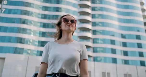 Νεαρή γυναίκα σε μια μεγάλη πόλη το καλοκαίρι κοιτάζει σε διαφορετικές κατευθύνσεις — Αρχείο Βίντεο