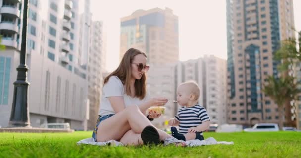Летом в парке мама кормит ребенка из контейнера обедом — стоковое видео