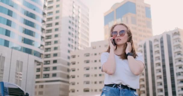 Fiatal gyönyörű nő beszél a telefonon a háttérben az épületek — Stock videók
