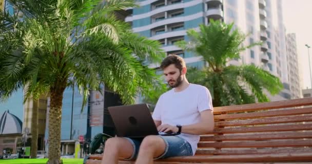 Młody mężczyzna w lecie palmy siedzi z laptopem i wpisując na klawiaturze — Wideo stockowe