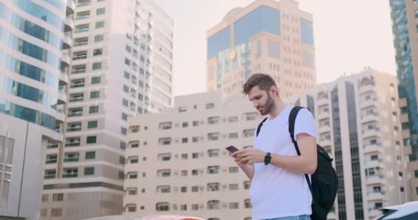 Egy fiatal férfi egy hátizsák és egy okostelefon a kezében — Stock videók