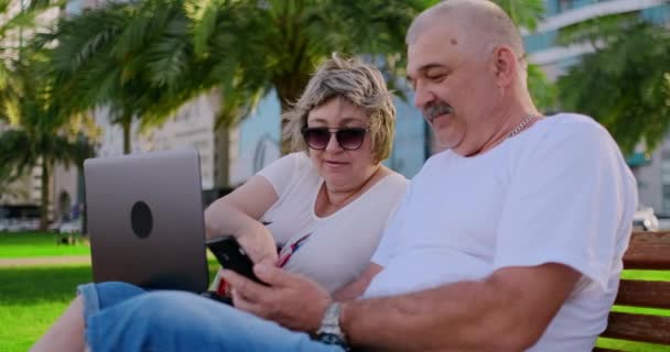 Starsza para za pomocą laptopa w parku w słoneczny dzień — Wideo stockowe