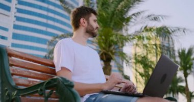 Palmiye ağaçlarının yazında genç bir adam bir dizüstü bilgisayar ile oturan ve klavyede yazarak