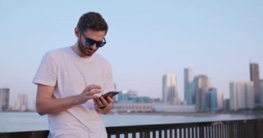Kamera, yakışıklı genç adamın telefonunu kullanırken etrafta dolaşıyor. Portre. Bulanık arka plan