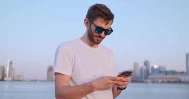 Kamera, yakışıklı genç adamın telefonunu kullanırken etrafta dolaşıyor. Portre. Bulanık arka plan