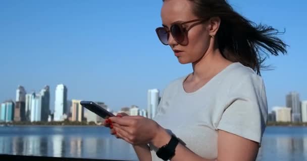 Une fille aux cheveux longs compose un message sur le smartphone au quai de Dubaï . — Video