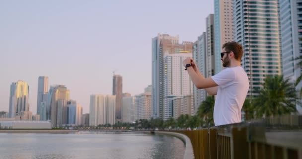 Un uomo in estate in piedi sul lungomare fotografato su uno smartphone paesaggio della città — Video Stock