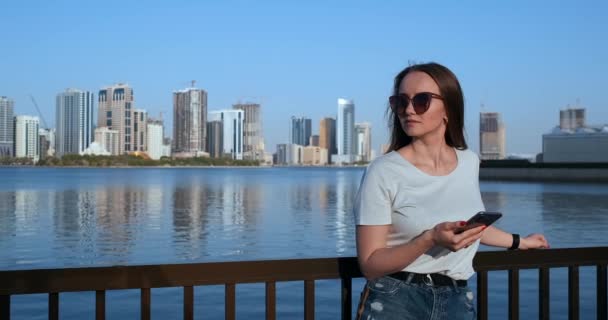 Una ragazza con i capelli lunghi compone un messaggio sullo smartphone al molo di Dubai . — Video Stock