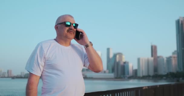 Senior homme debout sur le front de mer en été parler au téléphone — Video