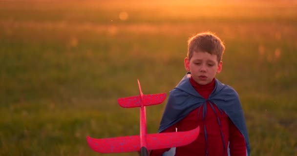 The boy runs across the field with a plane in his hands at sunset — Stock Video