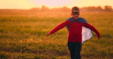 Süper kahraman kostümü ve maskeli çocuk gün batımında tarlada rüya ve fantezi