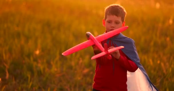 Chico jugando en el campo con un avión en sus manos al atardecer — Vídeos de Stock