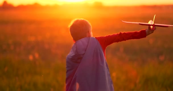 Jonge jongen piloot en loopt in het veld bij zonsondergang en spelen met vliegtuig dromen — Stockvideo