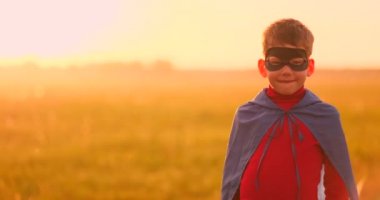 Gün batımında bir tarlada duran kameraya bakan bir süper kahraman maskesi bir çocuk portresi.