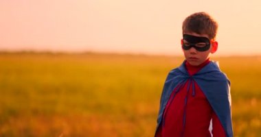 Gün batımında bir tarlada duran kameraya bakan bir süper kahraman maskesi bir çocuk portresi.