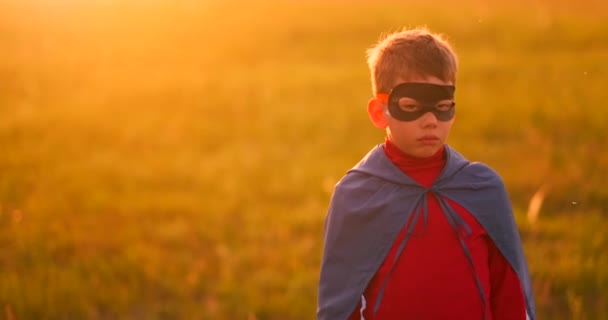 A gyermek a ruha egy szuperhős, egy piros köpenyt fut át a zöld gyepen, a háttérben a naplemente, a kamera felé