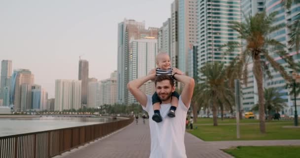 Молодий батько ходить з дитиною, сидячи на шиї влітку — стокове відео