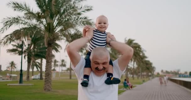 Abuelo mayor caminando con un niño sentado en el cuello en el verano — Vídeo de stock