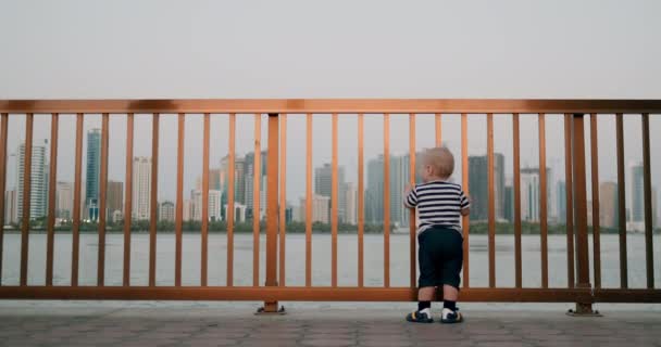 Baby schattig dansen houden handen op de reling aan de waterkant in de achtergrond van de stad — Stockvideo