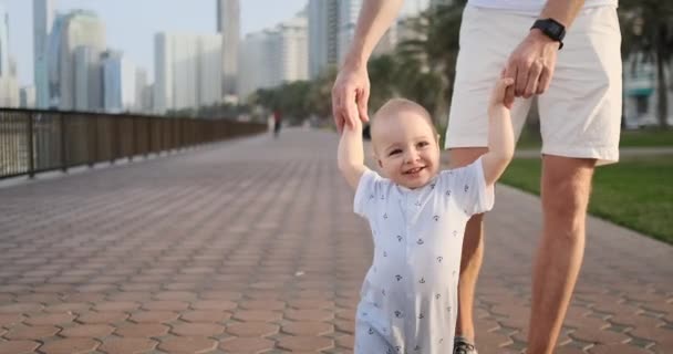 Young father with a child and first steps. Young father with a child at outdoor learninig for a first steps near urban in the city — Stock Video