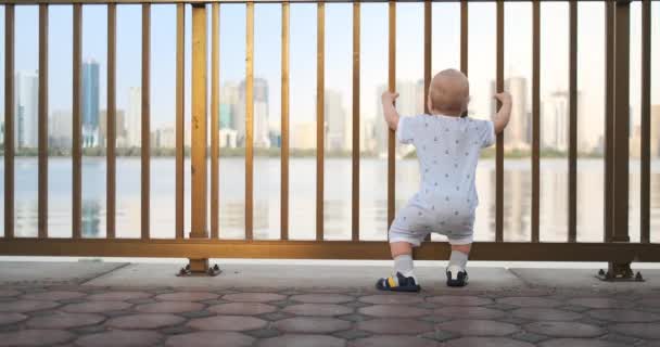 Bailando alegre chico europeo cerca de la valla mantiene ha barandilla y baile de pie y mirando a la vista del paseo marítimo en el verano en los Emiratos Árabes Unidos — Vídeos de Stock