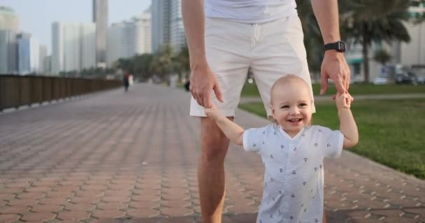 Young father with a child and first steps. Young father with a child at outdoor learninig for a first steps near urban in the city — Stock Video