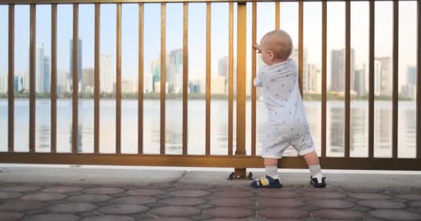 Dancing glada Europeiska pojke nära stängslet håller ha räcke och dans stående och titta på utsikten över strandpromenaden på sommaren i Förenade Arabemiraten — Stockvideo