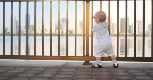 Bailando alegre chico europeo cerca de la valla mantiene ha barandilla y baile de pie y mirando a la vista del paseo marítimo en el verano en los Emiratos Árabes Unidos — Vídeos de Stock