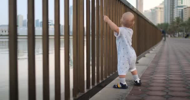 Danse joyeux garçon européen près de la clôture garde ha rambarde et danse debout et en regardant la vue sur la promenade en été aux EAU — Video