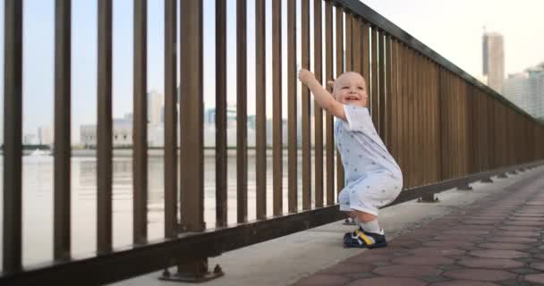 Bailando alegre chico europeo cerca de la valla mantiene ha barandilla y baile de pie y mirando a la vista del paseo marítimo en el verano en los Emiratos Árabes Unidos — Vídeos de Stock