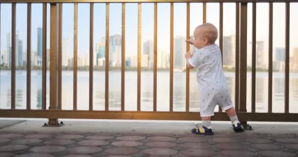 在围栏附近跳舞的欢快的欧洲男孩保持哈栏杆和舞蹈站立,看着在阿联酋的夏天的长廊的景色 — 图库视频影像