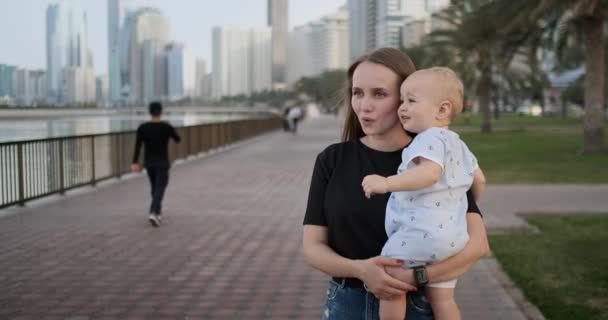 No verão, uma jovem mãe caminhando com uma criança ao longo do passeio — Vídeo de Stock