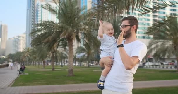 Baba yaz aylarında oğulları ile palmiye ağaçları ve binalar etrafında oynuyor — Stok video
