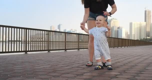 Sorrindo Menino segurando a mão de suas mães faz os primeiros passos andando ao longo do passeio no verão — Vídeo de Stock