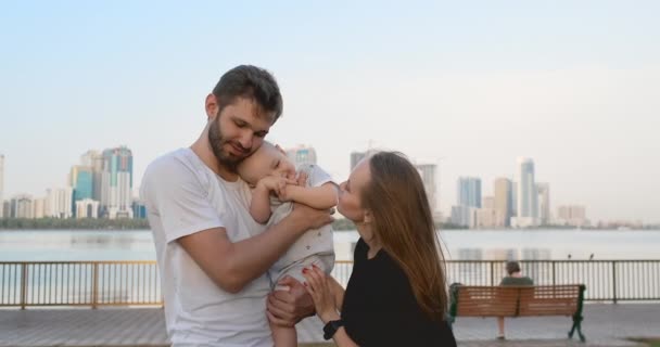 Stad föräldrar pappa mamma höja sin son som står på vattnet i bakgrunden av staden — Stockvideo