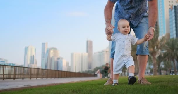 Jonge vader met een kind en eerste stappen. Jonge vader met een kind op outdoor learninig voor een eerste stappen in de buurt van Urban in de stad — Stockvideo
