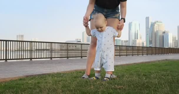 Smiling Boy holding his mothers hand makes the first steps walking along the promenade in the summer — Stock Video