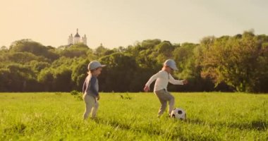 İki erkek bir futbol topu ile oynarken gülüyor ve sahada gün batımında gülümseyerek