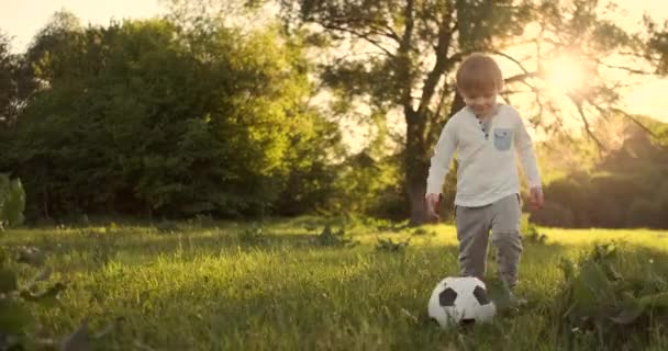 Niño feliz corriendo con pelota de fútbol corriendo al atardecer en el campo de verano — Vídeos de Stock