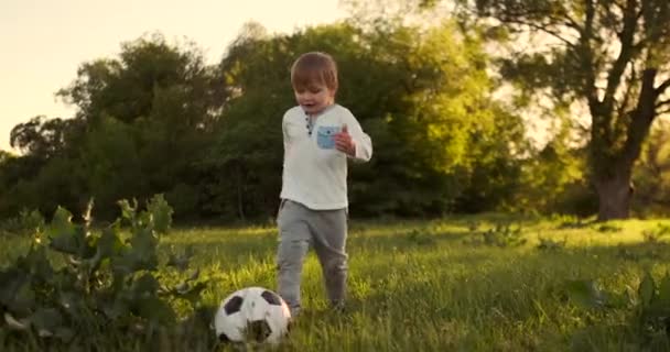 Niño feliz corriendo con pelota de fútbol corriendo al atardecer en el campo de verano — Vídeo de stock