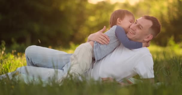 Liebender Vater und Sohn umarmen sich bei Sonnenuntergang im Gras in Zeitlupe — Stockvideo