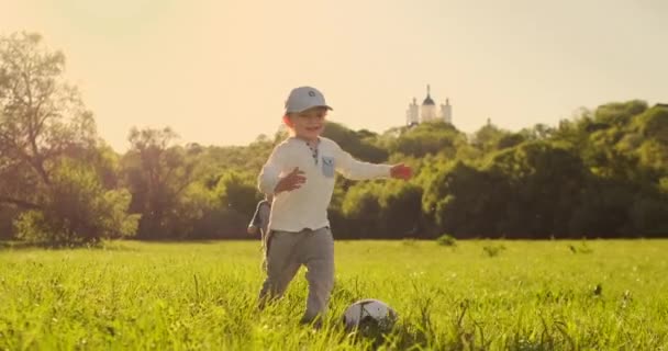 El chico corre con una pelota de fútbol riéndose al atardecer en cámara lenta — Vídeo de stock
