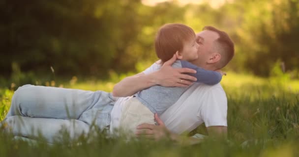 Pai e filho abraçando deitado no prado ao pôr do sol — Vídeo de Stock