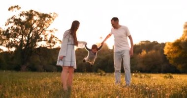 Anne ve baba elleri üzerinde oynarken çocuk sallamak, çocuk gün batımında sokakta anne ve babası ile oynarken mutlu