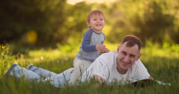 Αγαπώντας νεαρό πατέρα και γιο παίζουν στο γρασίδι το καλοκαίρι στο ηλιοβασίλεμα σε αργή κίνηση — Αρχείο Βίντεο