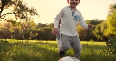 Yavaş çekimde, futbol topu olan mutlu bir çocuk gün batımında profesyonel futbol oynamahayaliyle sahaya koşar.