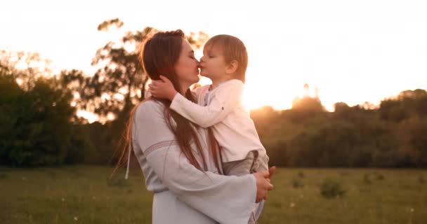 Niño abrazando a la madre al atardecer en el verano, un hijo cariñoso y una familia feliz tocando — Vídeo de stock