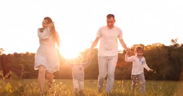 Gelukkige familie hun man met twee kinderen wandelen op het veld bij zonsondergang in de zonsondergang licht in de zomer in warm weer — Stockvideo