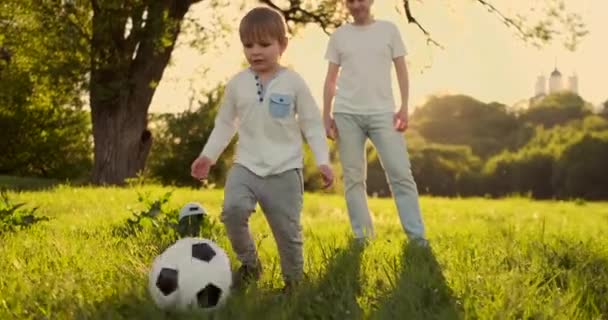 Отец и ребенок играют в футбол, стоя на поле на закате. Мальчик забивает гол. Отец вратаря у ворот, ребенок бьет по мячу. — стоковое видео