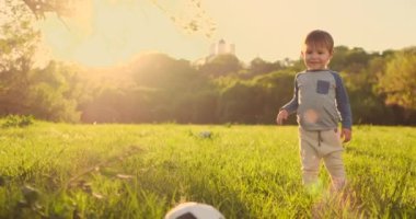 Gün batımında bir futbol topu ile çim üzerinde duran çocuk